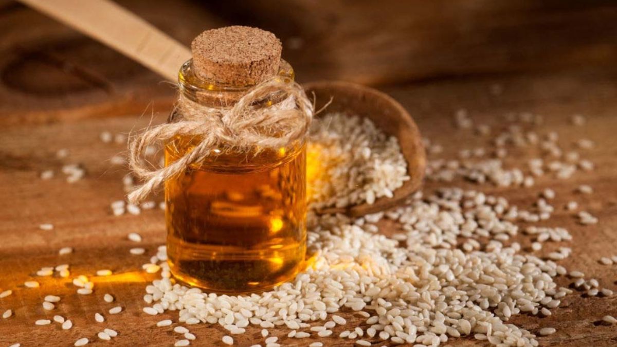 sesame oil in a small bottle pictured next to a wooden spoonful of sesame seeds spilling out