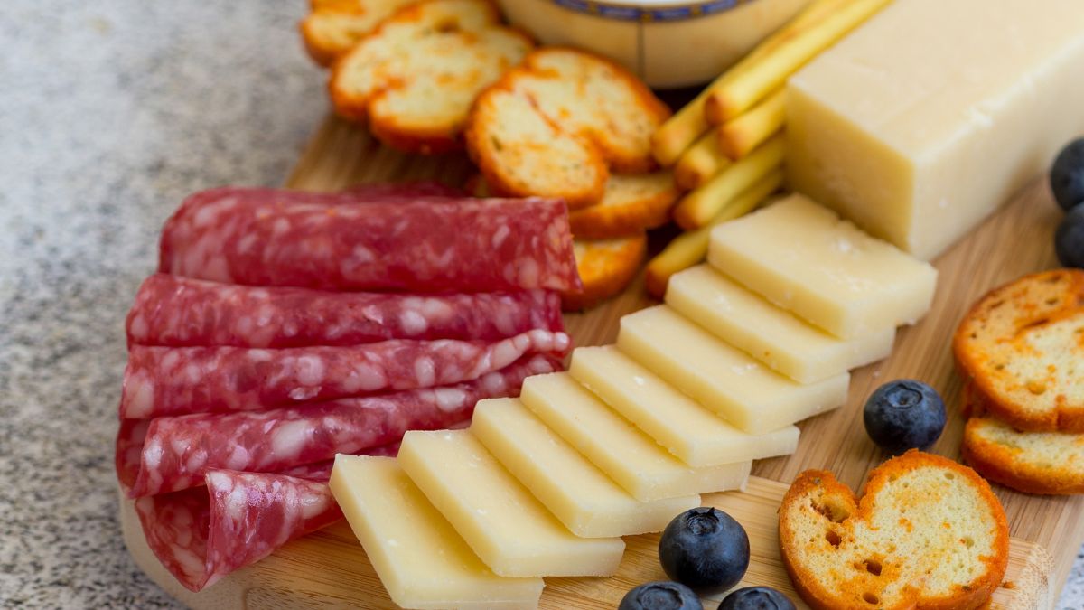 dry salami served on a wooden board with some bruschetta, cheese, and blueberries