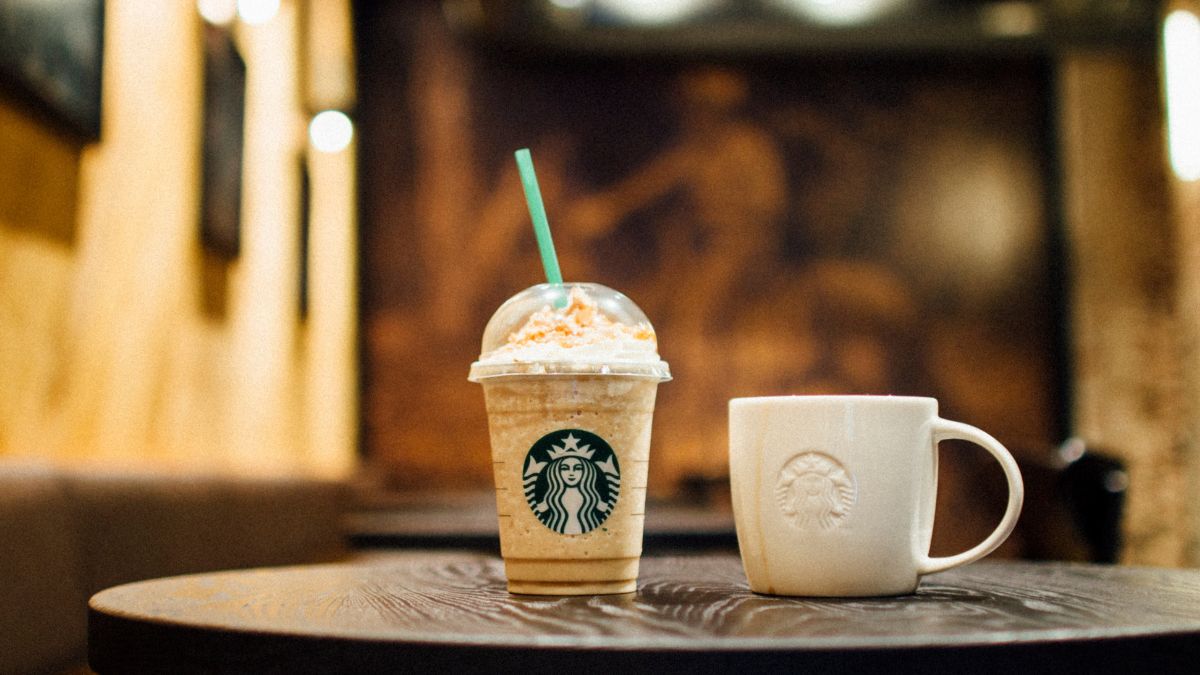 Starbucks Caramel Frappucino With Caramel Sauce on a table next to another cup with Starbucks logo