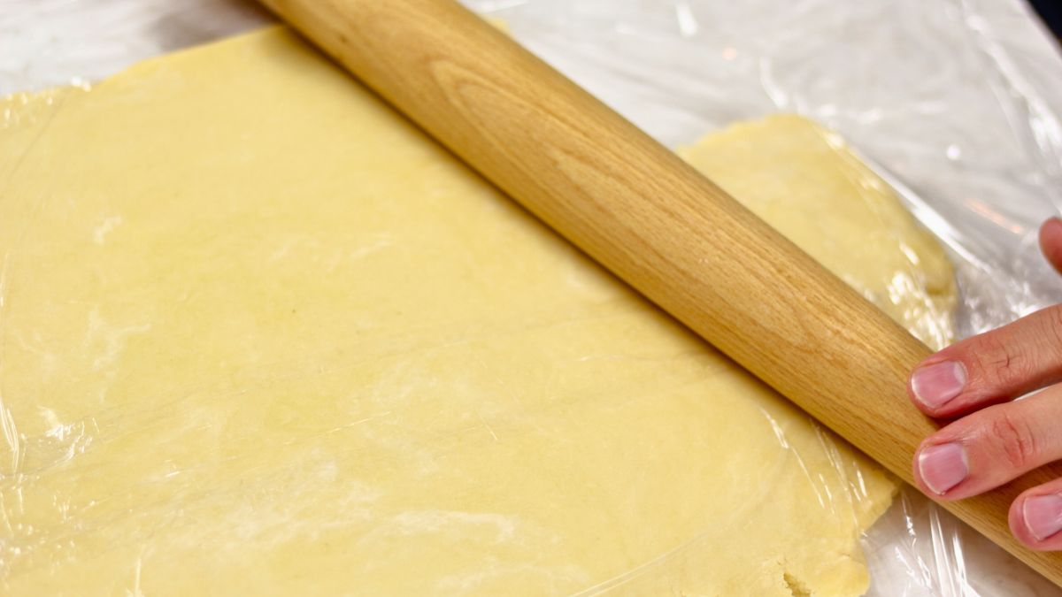 rolling out watery pie dough between two layers of plastic foil